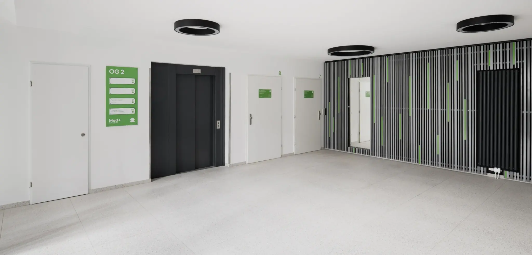 Offenes, helles Treppenhaus mit modernem Geländer, großen Fenstern und Wegweiser für die Etagen.